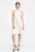 Model wearing cream satin mini dress with halter neck and open back, holding a small clutch.