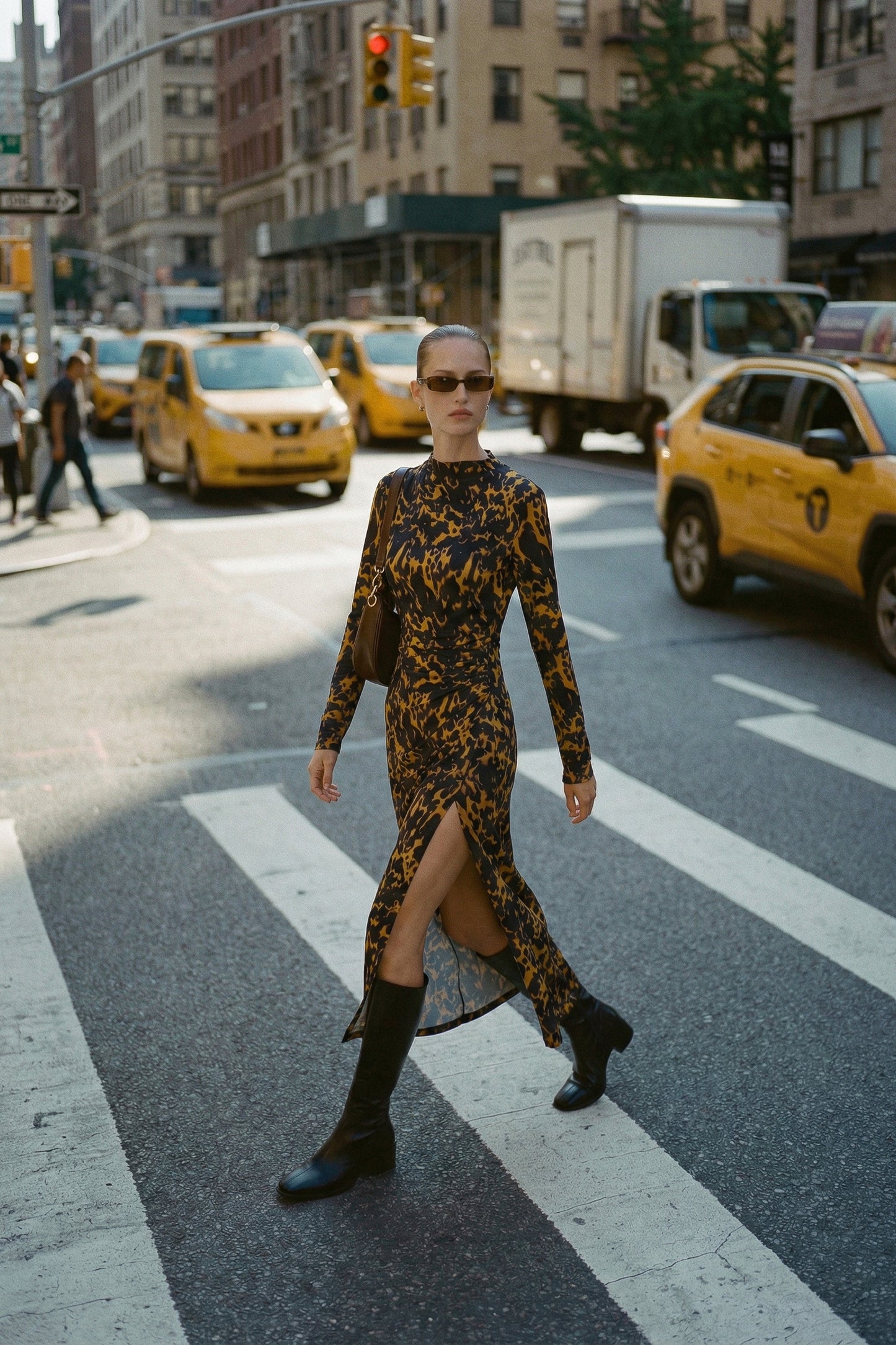 Woman in a patterned leopard print slit midi dress crossing a city street with taxis and traffic lights in the background.