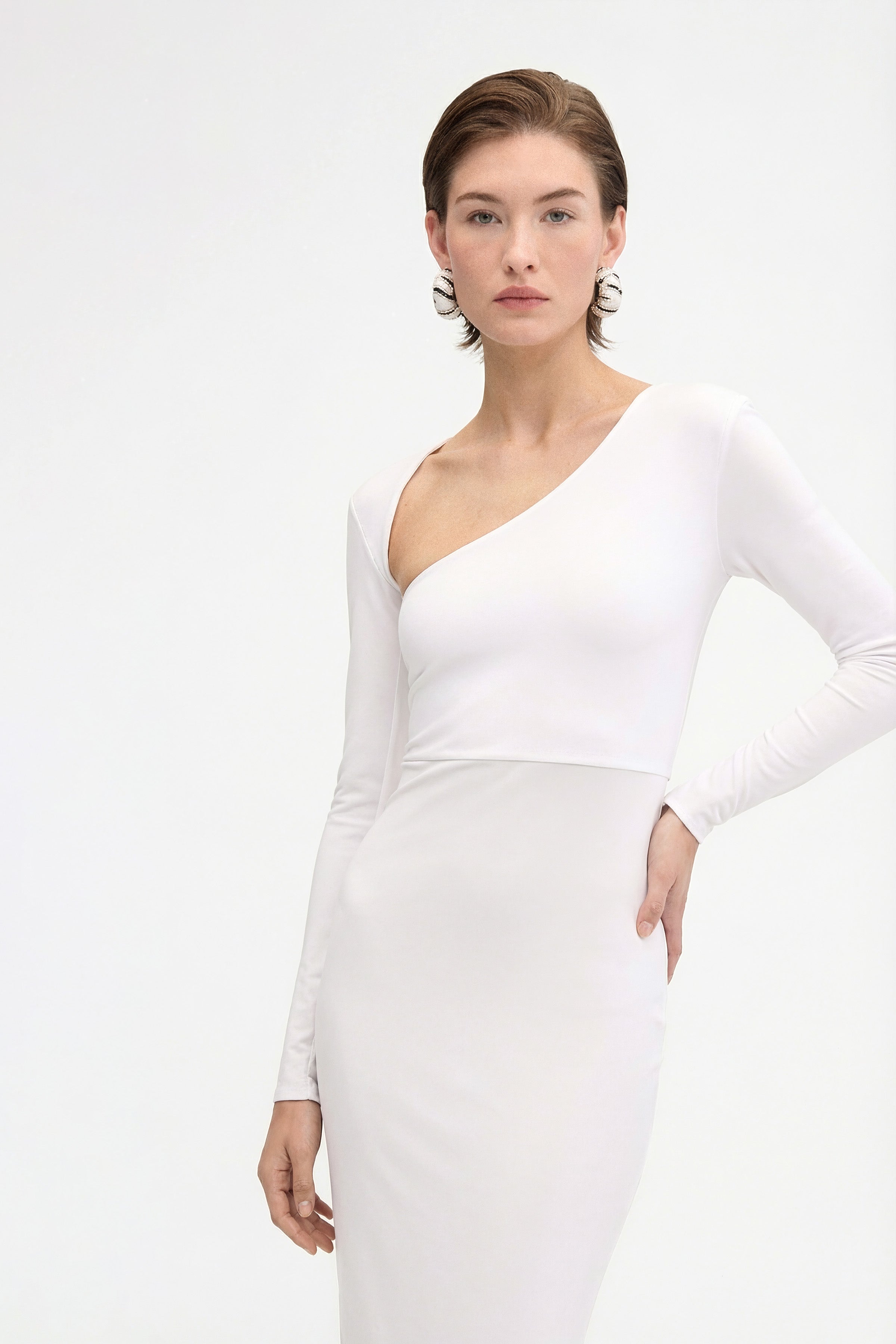 Close-up of the bodice of a white asymmetric long-sleeve dress highlighting the diagonal neckline and minimalist fitted design.