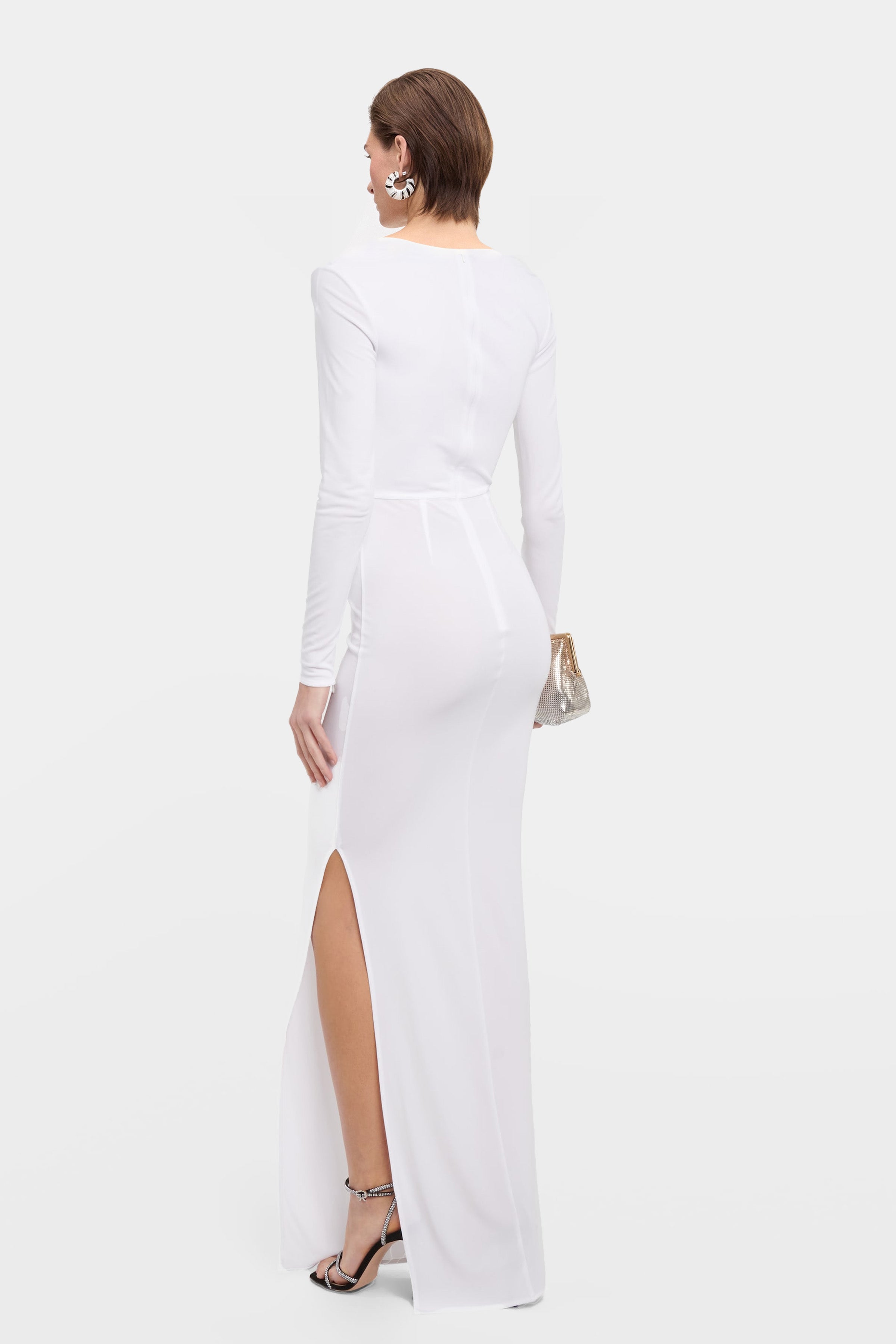 Rear view of a fitted white long-sleeve formal dress showing the back seam detail, side slit, and elegant floor-length silhouette.