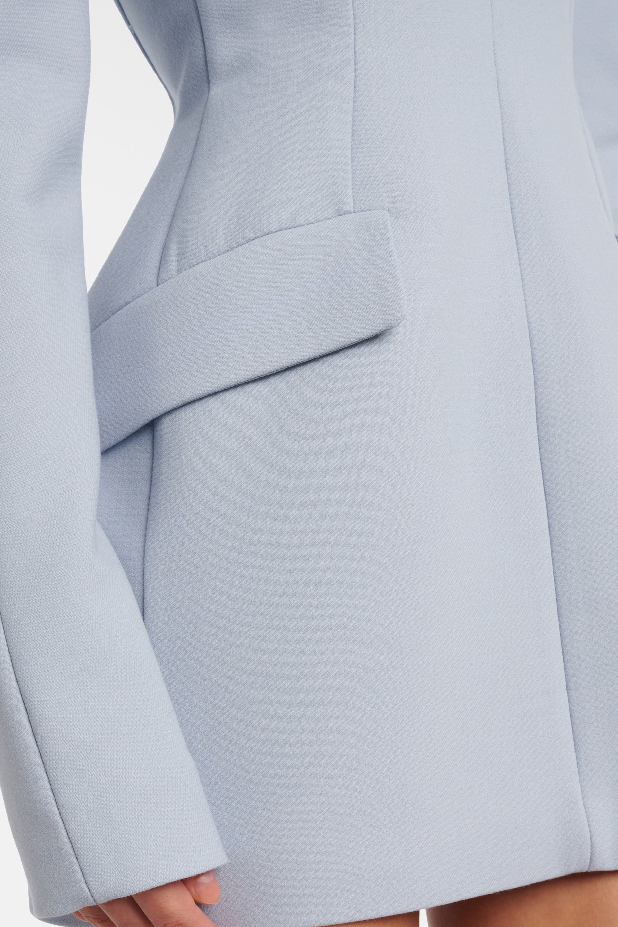 Close-up detail of the architectural hip flap and precision stitching on a structured light blue long-sleeve dress.