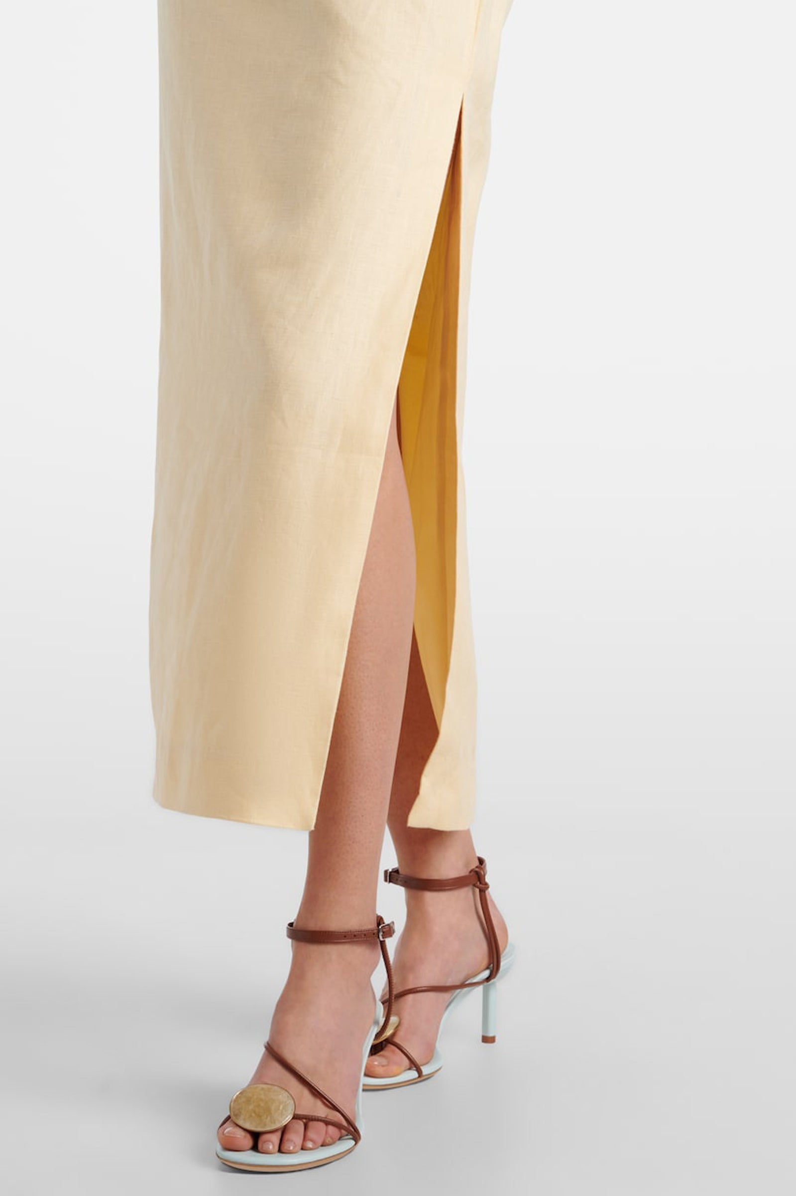 Close-up of the side slit on the yellow linen midi dress, revealing the model's leg and sandals.