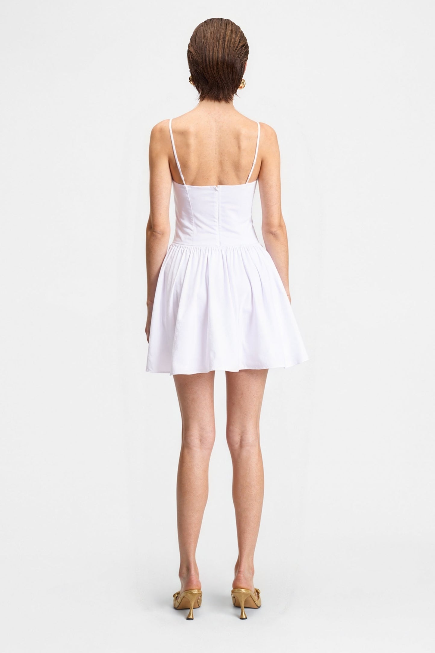 Back view of the white poplin cotton mini dress on a model, showing the delicate spaghetti straps and the gathered A-line skirt.