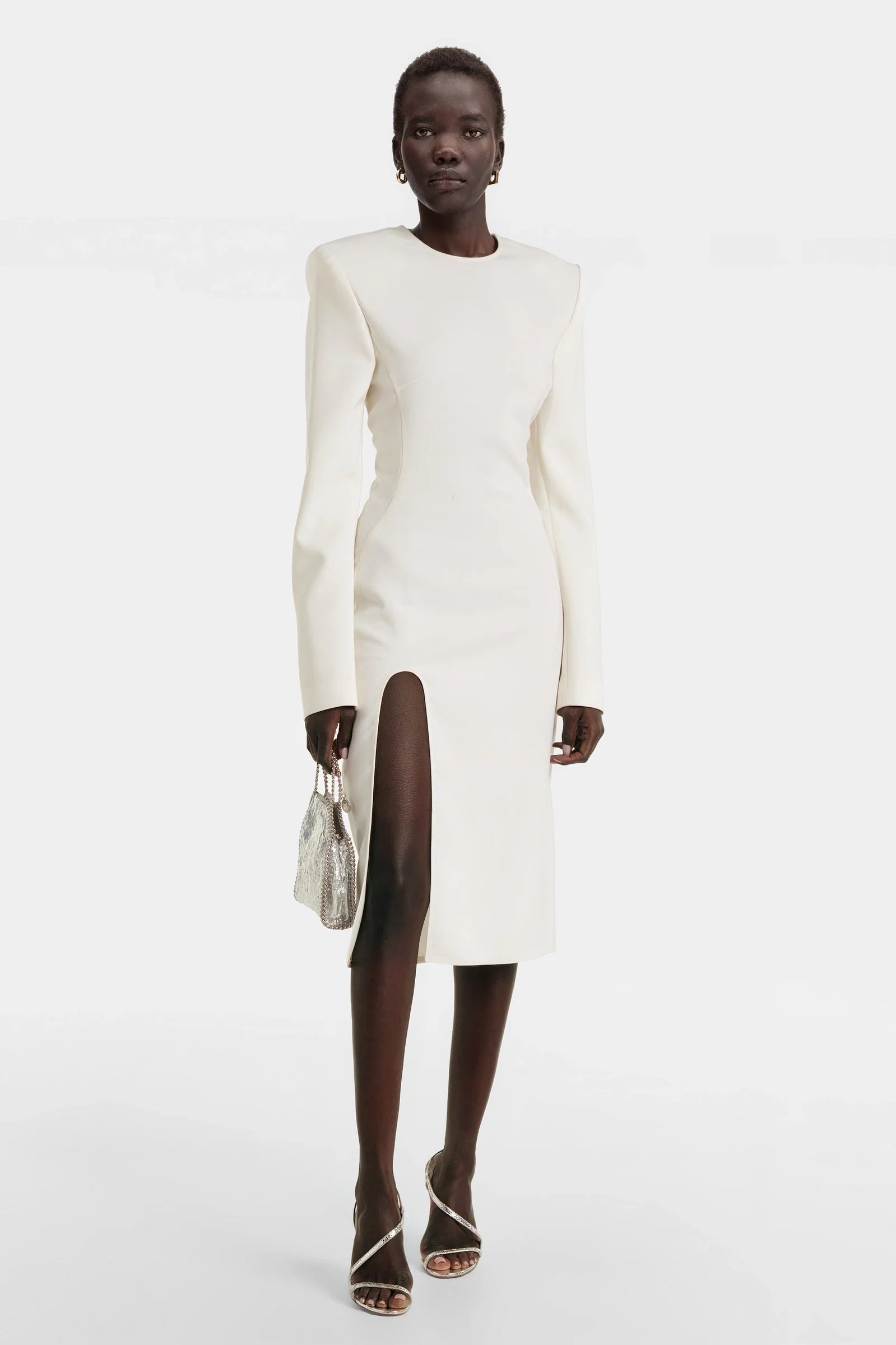 Model wearing white structured shoulder slit dress with silver bag and heels
