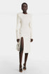 Model wearing white structured shoulder slit dress with silver bag and heels